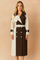 A stylish Australian woman with long ash blond hair wears a modern two-tone trench coat, posed against a softly lit warm sand and pastel pink background, ideal for chic autumn-winter fashion campaigns